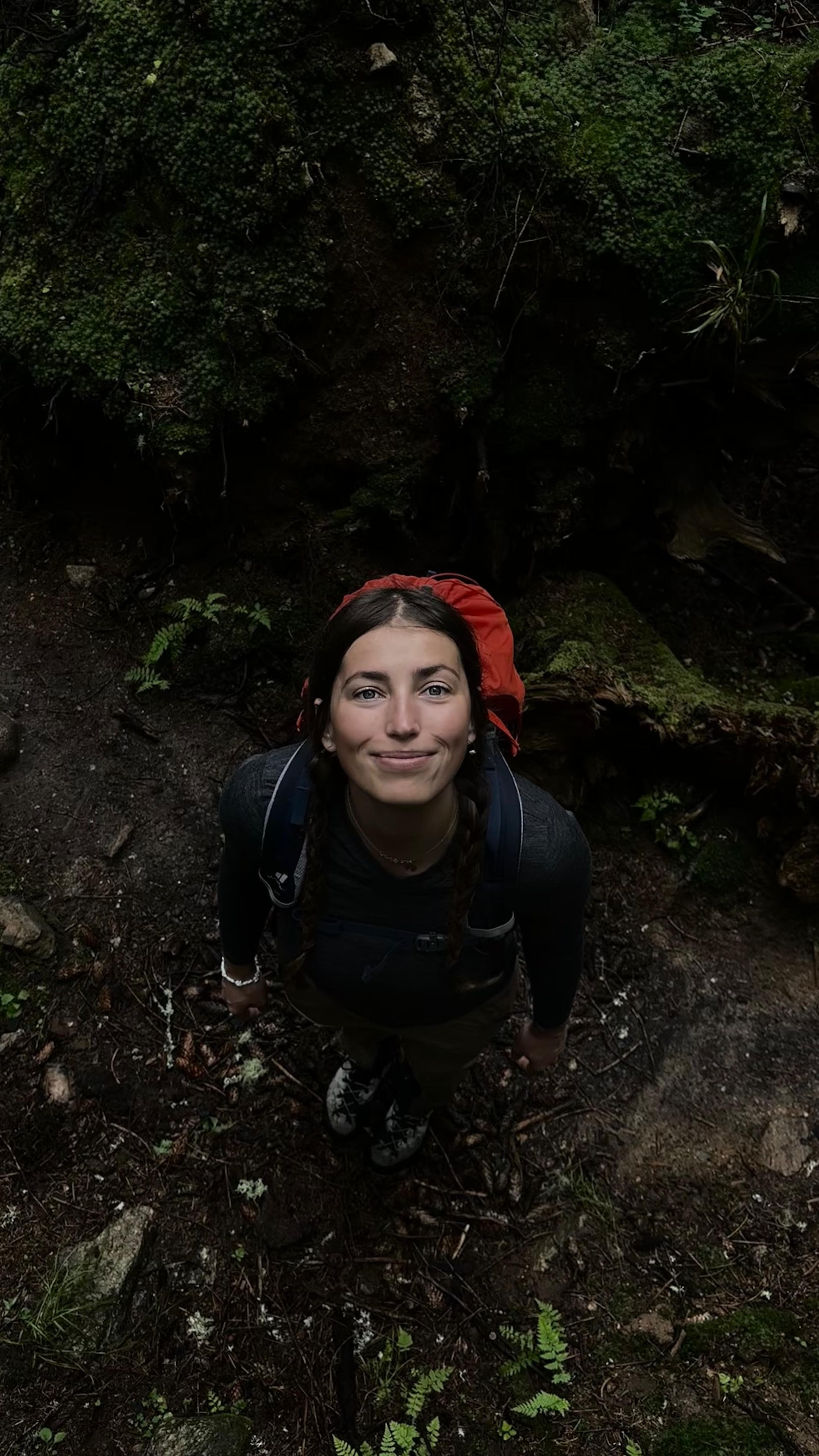 Kristína Turčanová looking up, in a mossy forest with her pack
