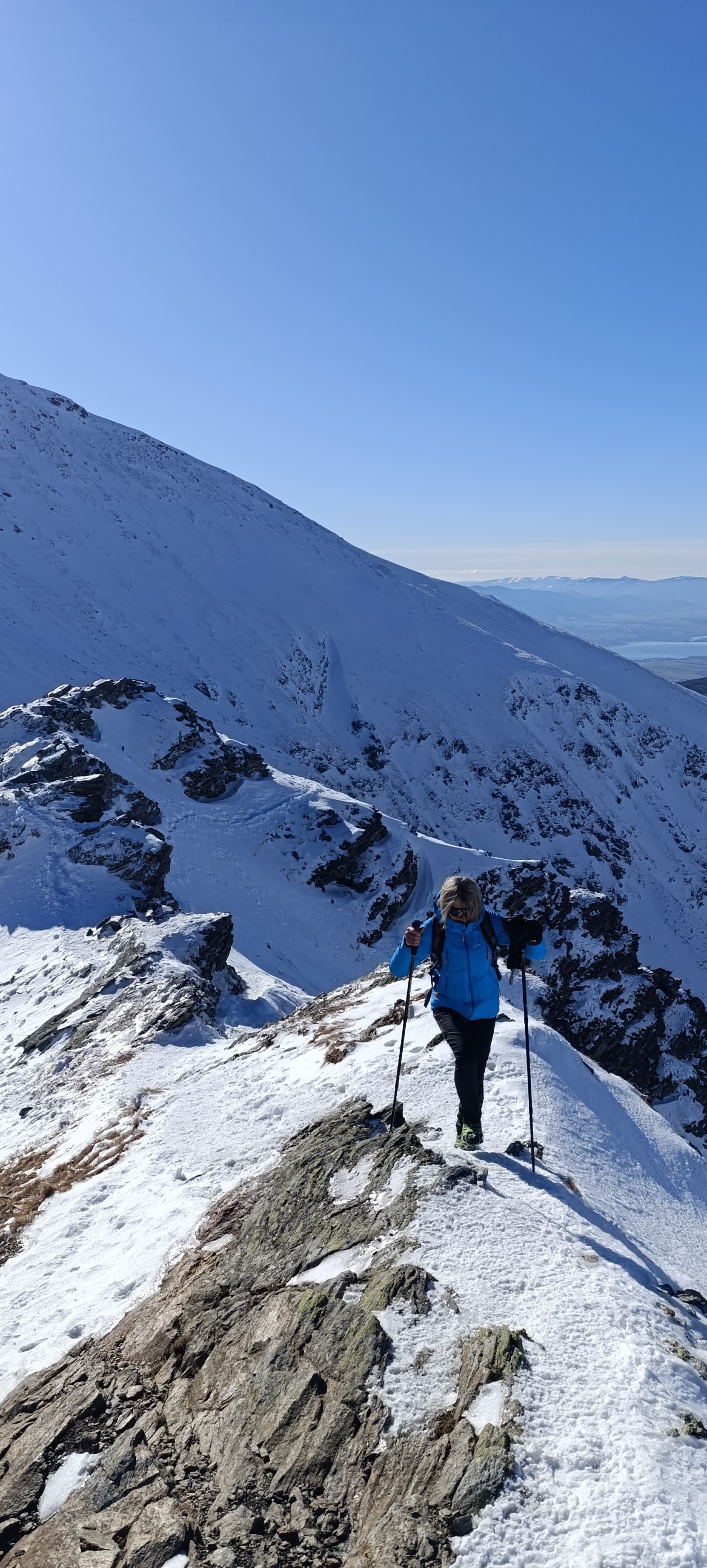 A walker climbing a snow-covered ridge under a clear winter sky